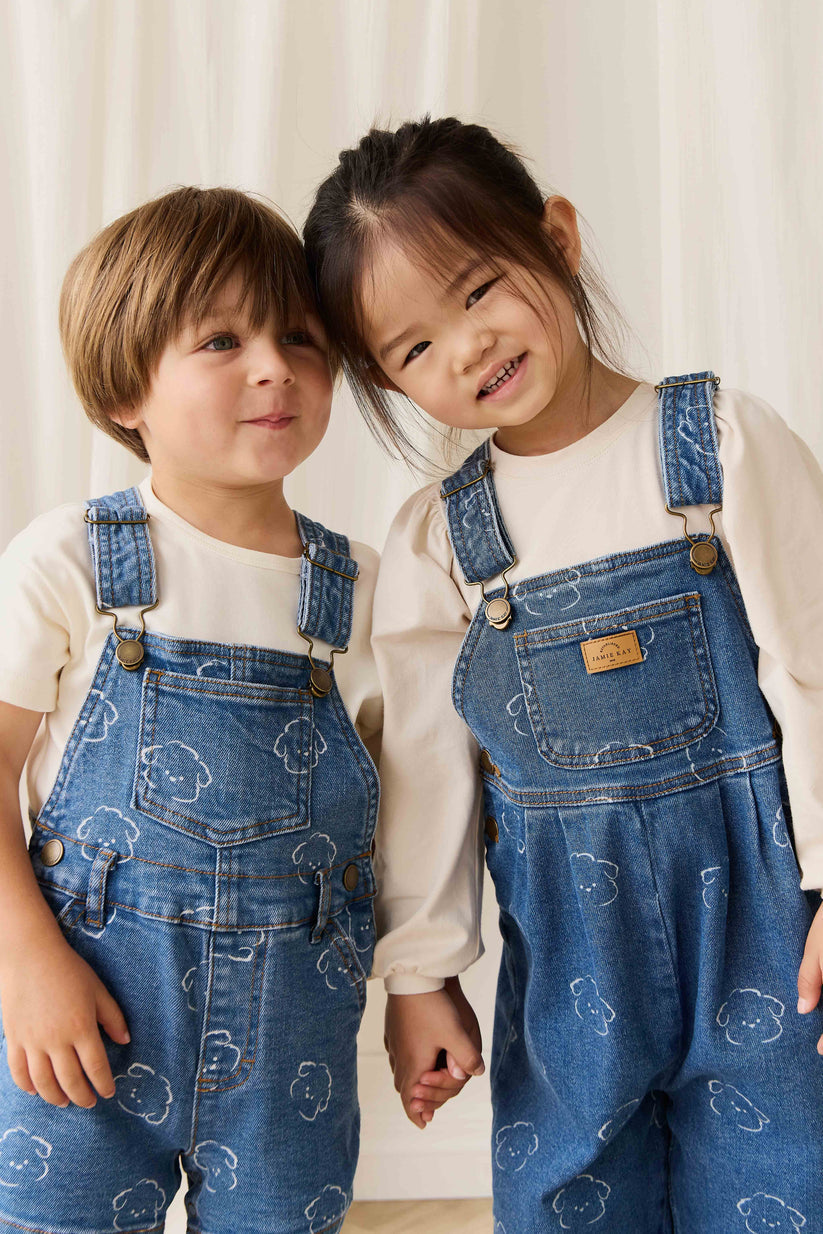 Two children wearing matching blue denim overalls with a white background