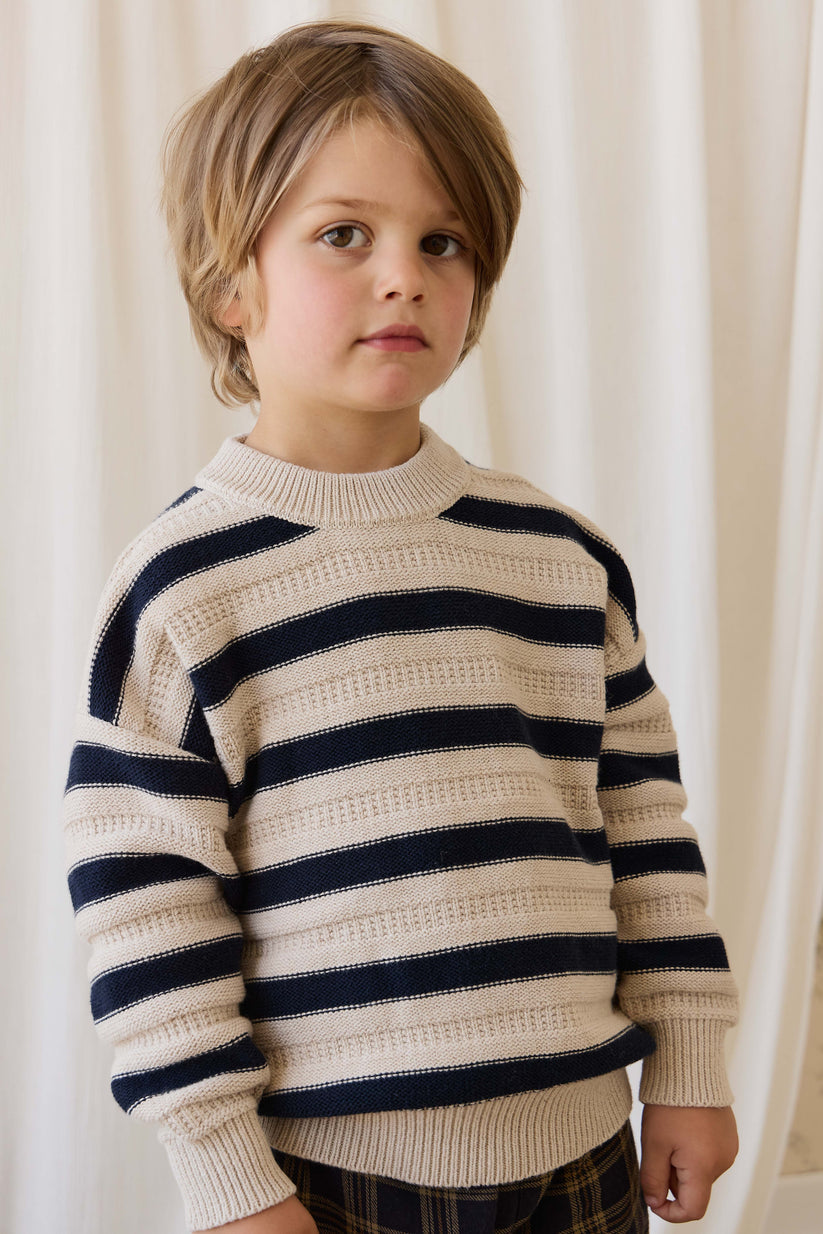 Child wearing a striped sweater against a white curtain background