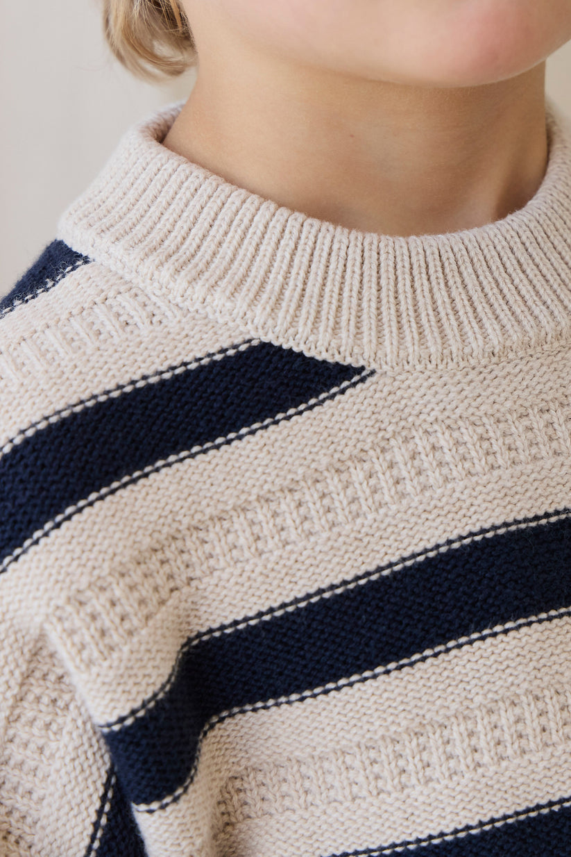 Close-up of a person wearing a beige sweater with navy blue stripes.