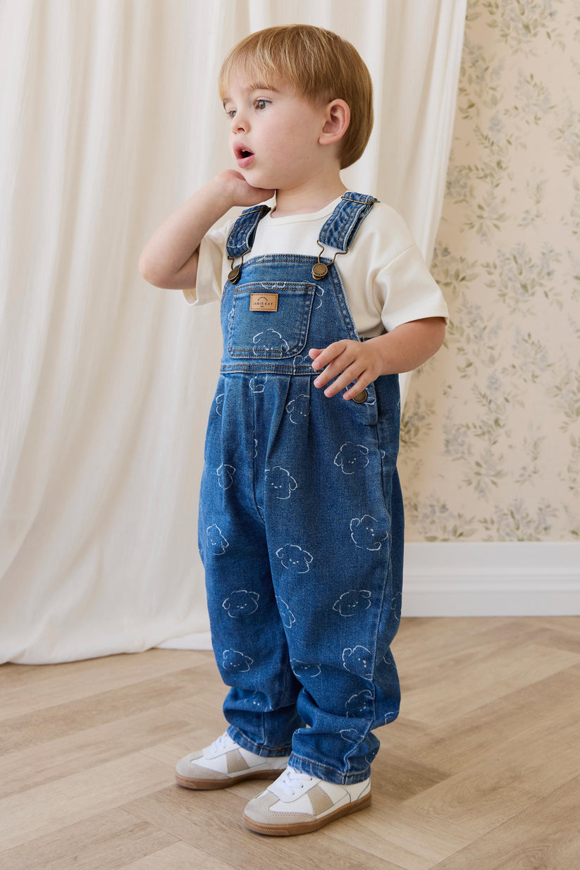 Child wearing blue denim overalls with a dog pattern indoors.