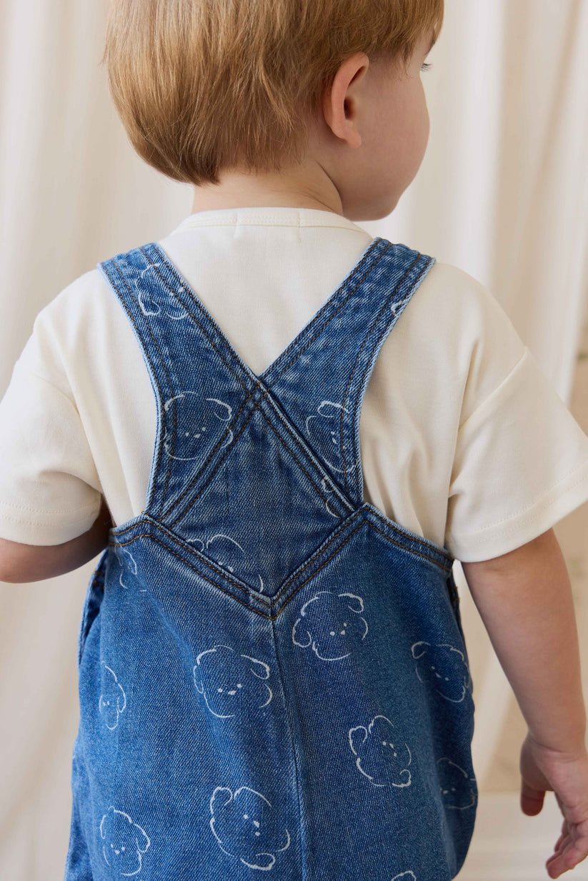 Child wearing a blue denim dress with bear patterns on a plain background