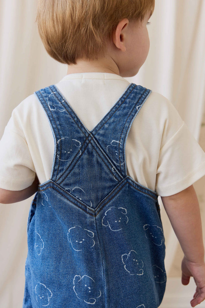 Child wearing a blue denim dress with bear patterns on a plain background