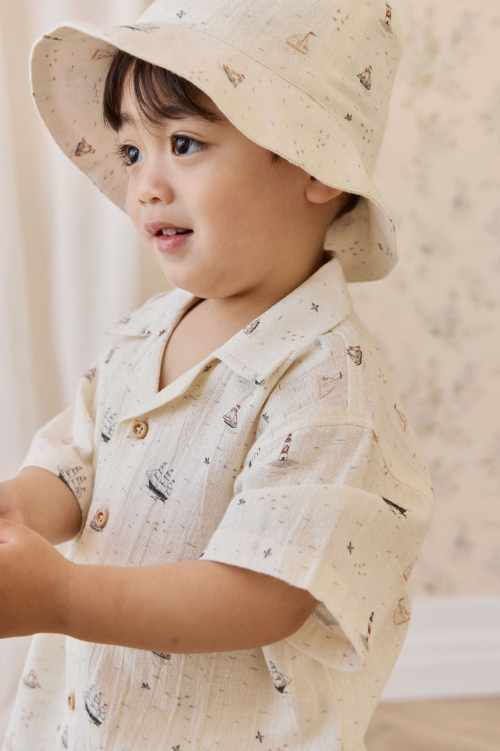 Child wearing a light-colored hat and shirt with a subtle pattern against a neutral background