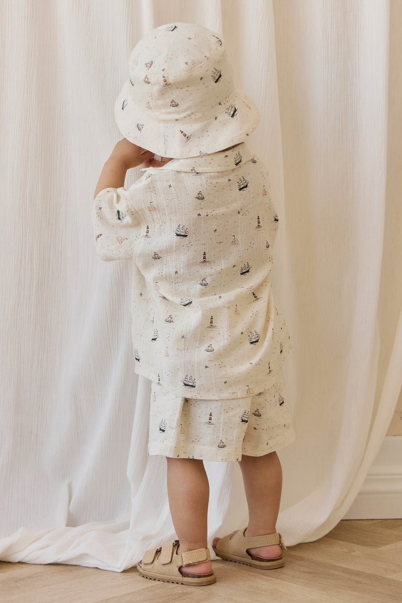 Child wearing a nautical patterned outfit and hat against a white curtain background
