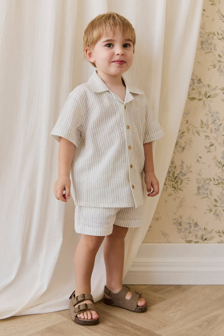 Child wearing a striped shirt and shorts set standing in front of a white curtain.
