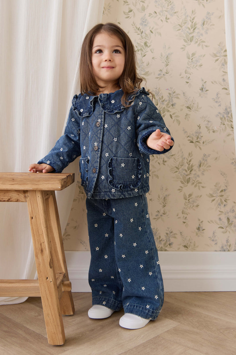Child wearing a denim outfit with white floral patterns standing on a wooden stool.