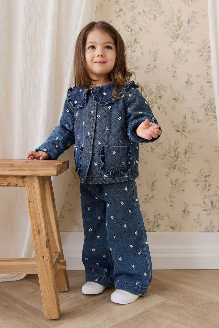 Child wearing a denim outfit with white floral patterns standing on a wooden stool.