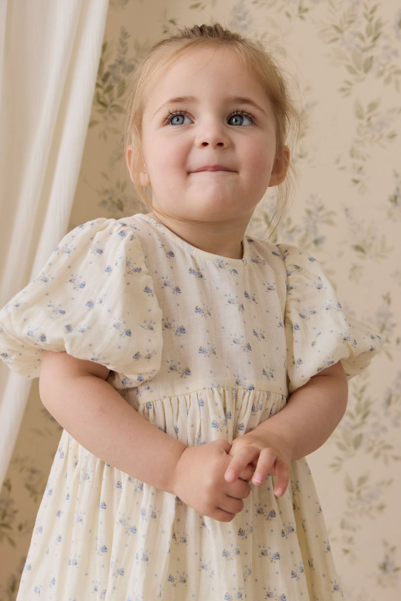 Young girl in a floral dress standing against a floral wallpapered wall.