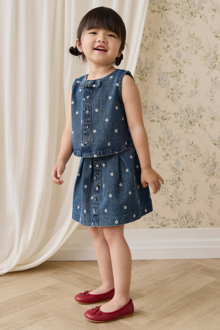 Young girl in a denim outfit standing in a room with floral wallpaper.
