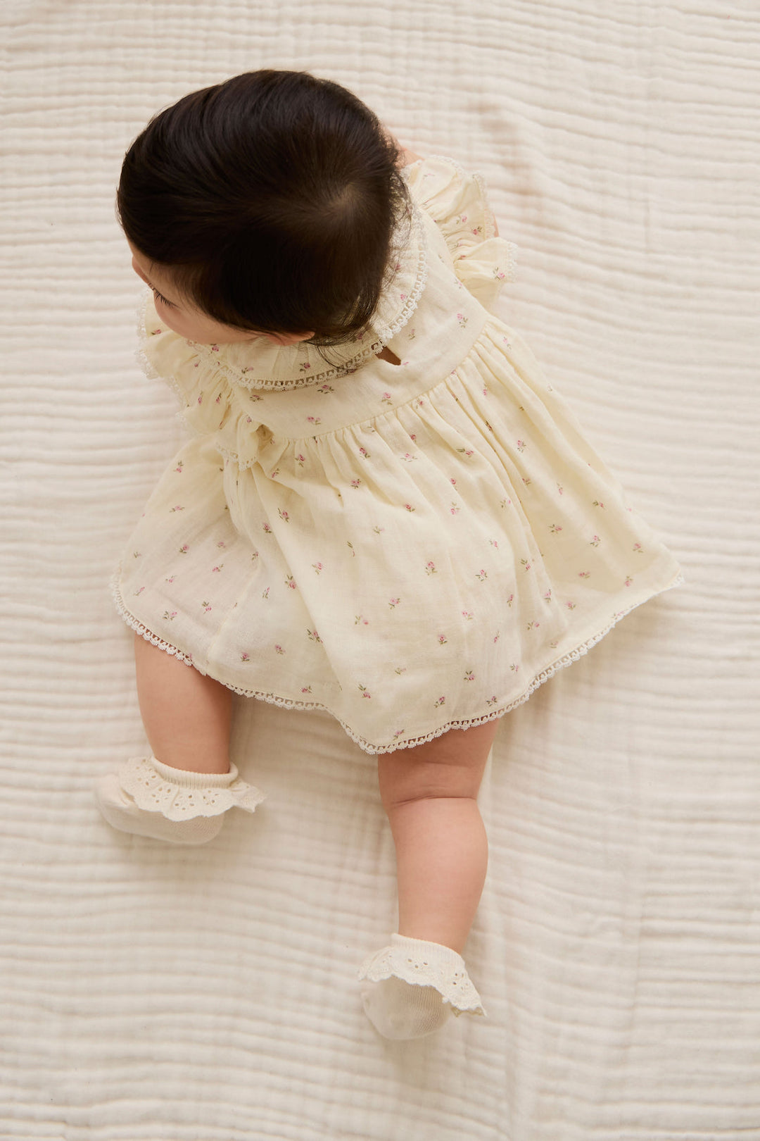 Baby in a white dress with subtle floral details lying on a textured white surface