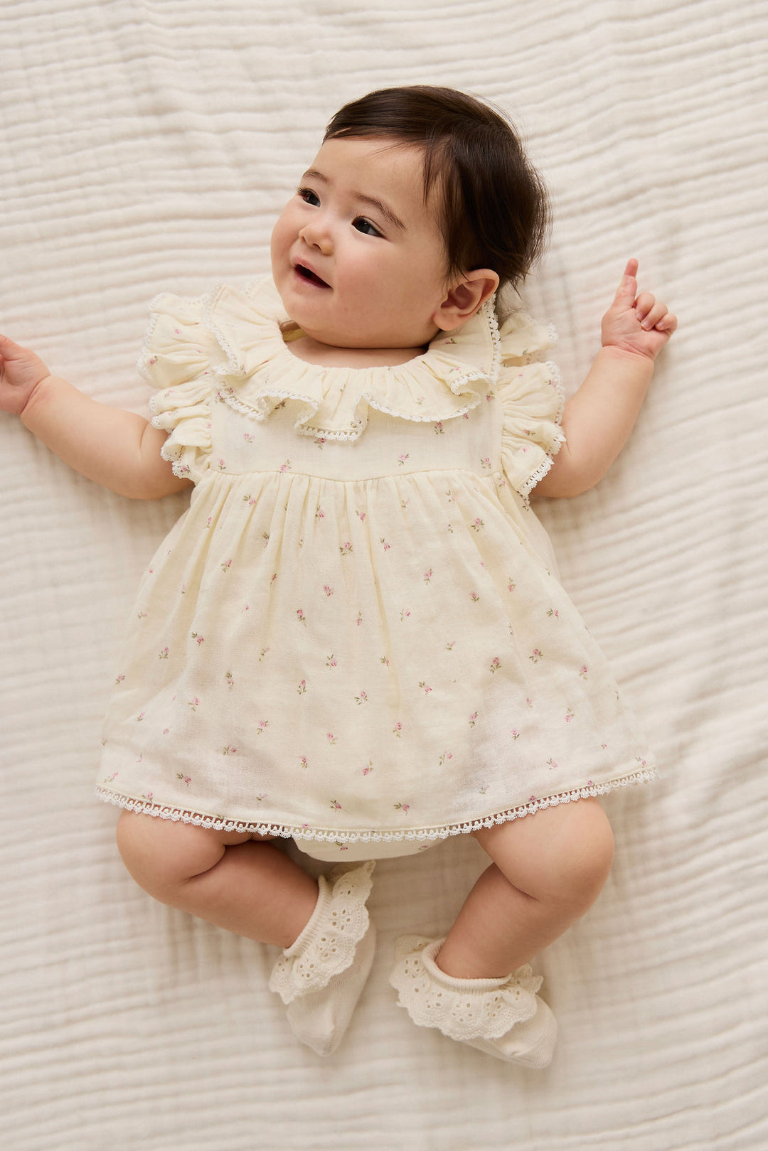 Baby in a white dress lying on a textured white surface
