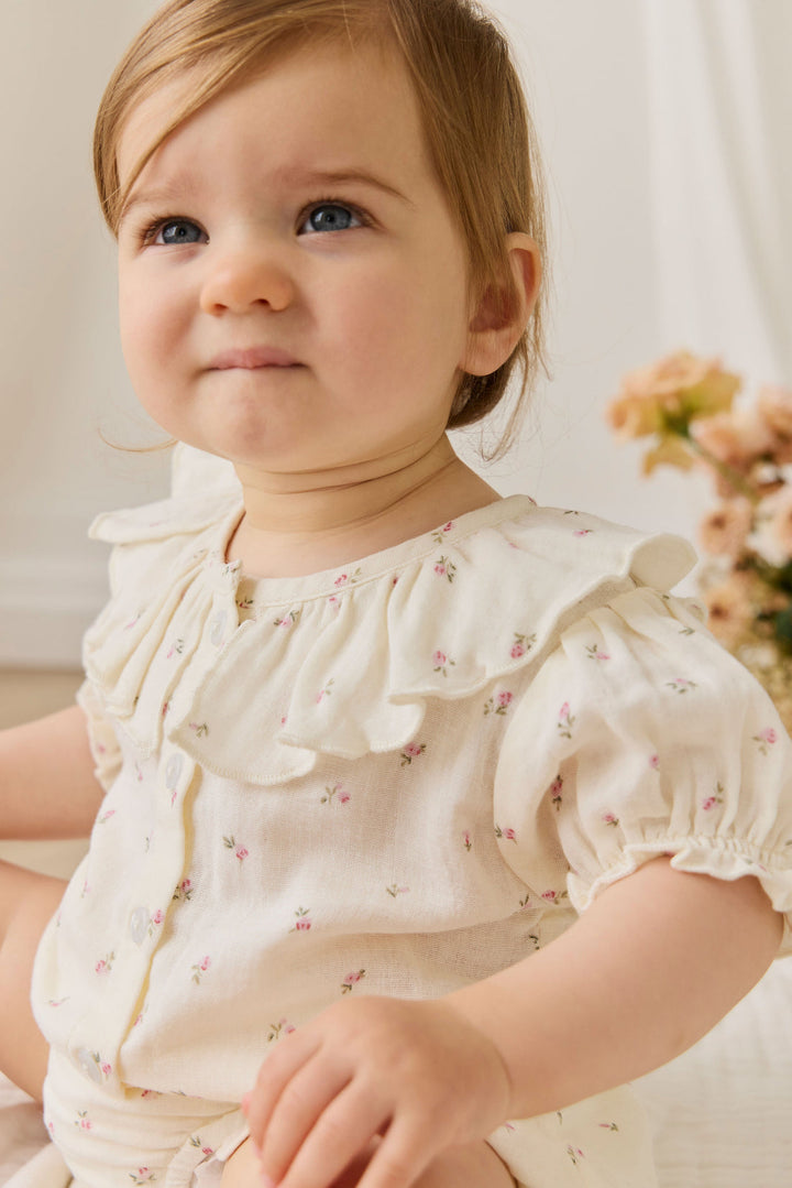 Young child wearing a white blouse with floral patterns, sitting indoors.