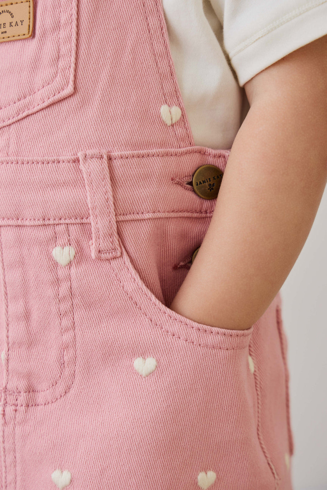 Close-up of pink denim overalls with heart patterns on a plain background