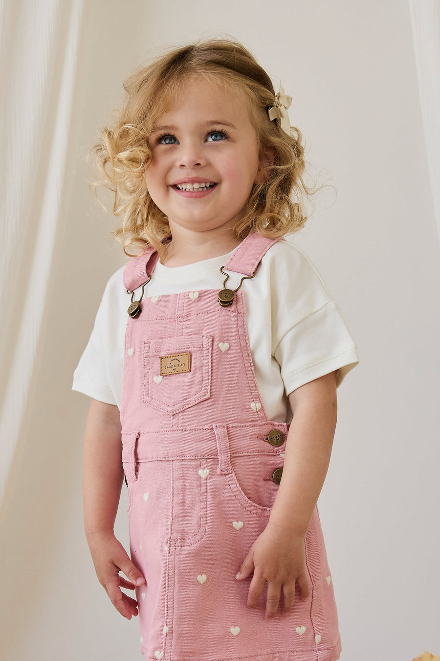 Young girl wearing a pink denim dress with heart patterns against a plain background