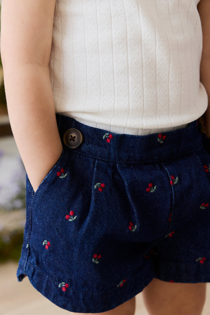 denim shorts with red and green cherry embroidery worn by a person, blurred background