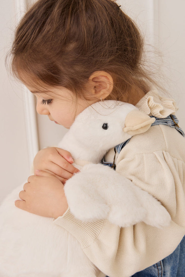 Child holding a white plush toy with a neutral background