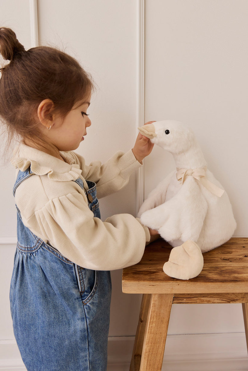 Child playing with a plush duck on a wooden table against a white wall.
