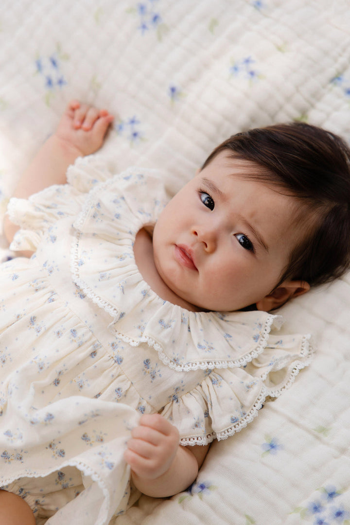 Baby in a white dress lying on a floral blanket