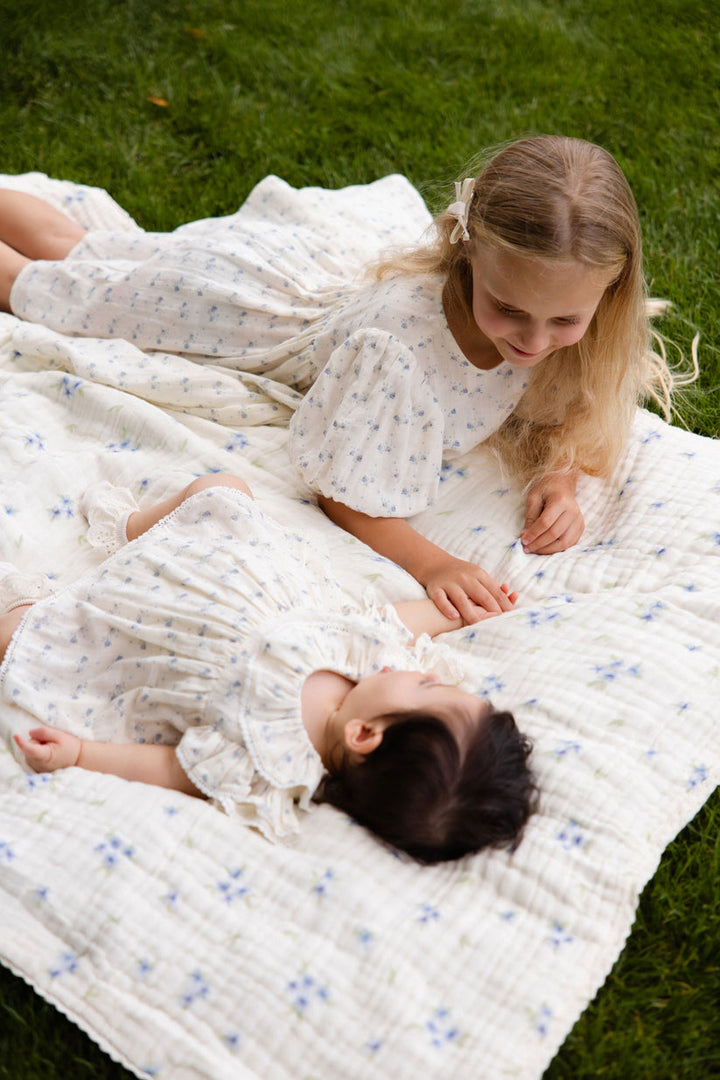 Two children lying on a white floral quilt in a grassy area