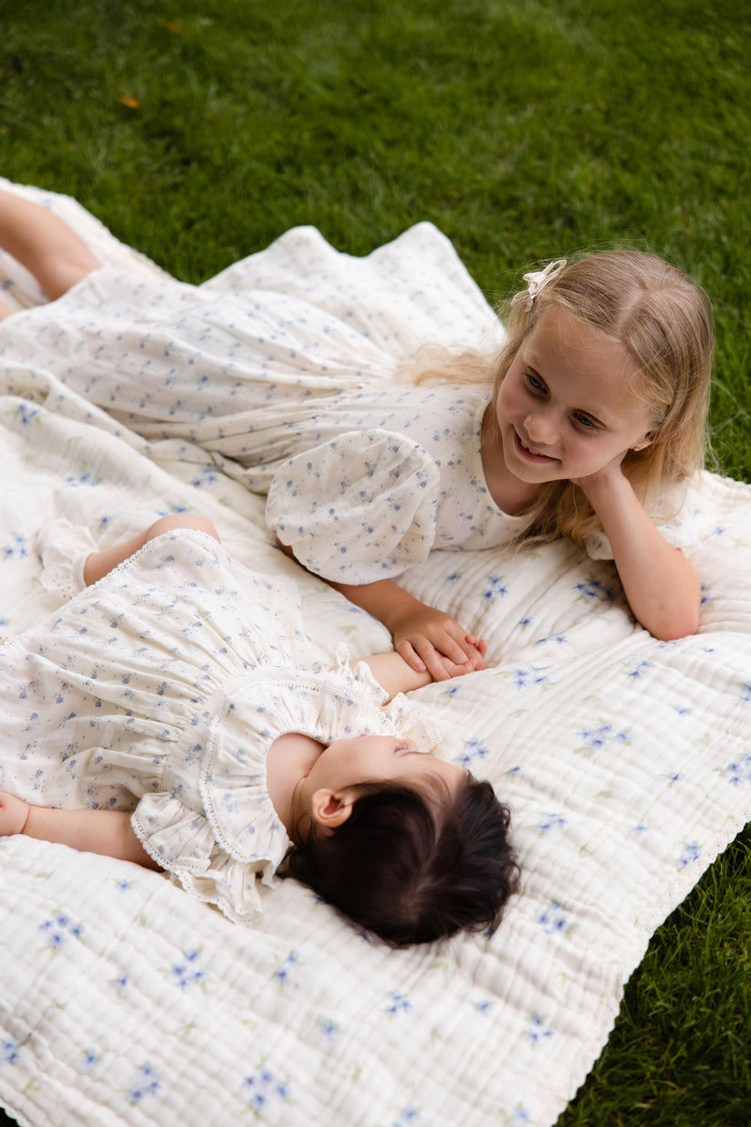 Two children lying on a floral blanket in a grassy area
