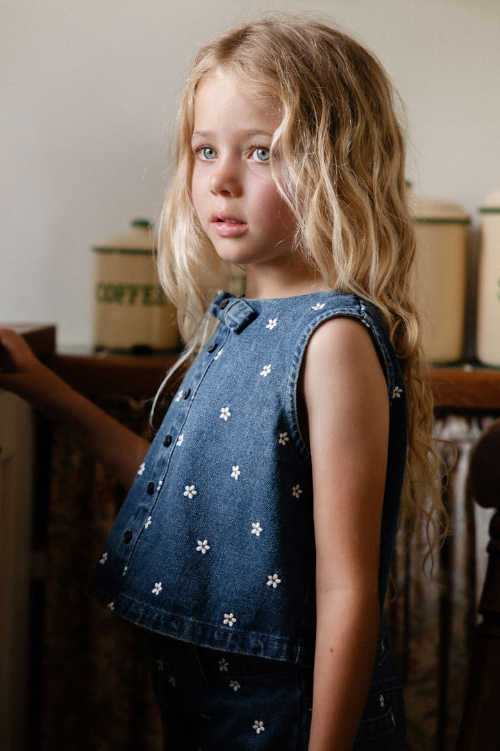 Young girl wearing a denim shirt with white floral patterns in an indoor setting.