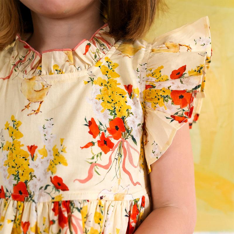 yellow dress with ruffle at the neck and sleeves. yellow flowers, bright orange flowers and chicks all over the dress. 