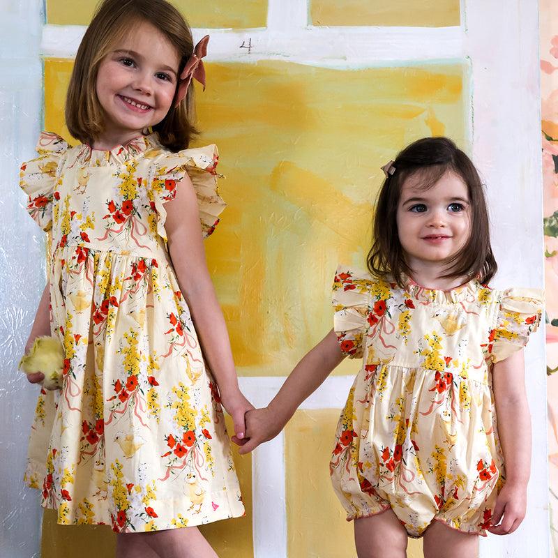two little girls modeling the baby chick outfits, one dress with ruffle at collar and sleeves and little sister wearing the bubble with ruffle on sleeves. 