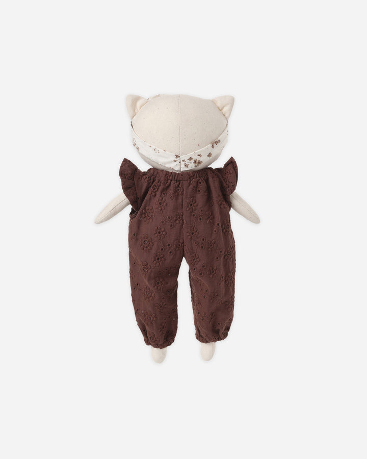 A plush cat doll viewed from the back, wearing a cream-colored cat hat with embroidered details and dark brown eyelet trousers, set against a plain light gray background.