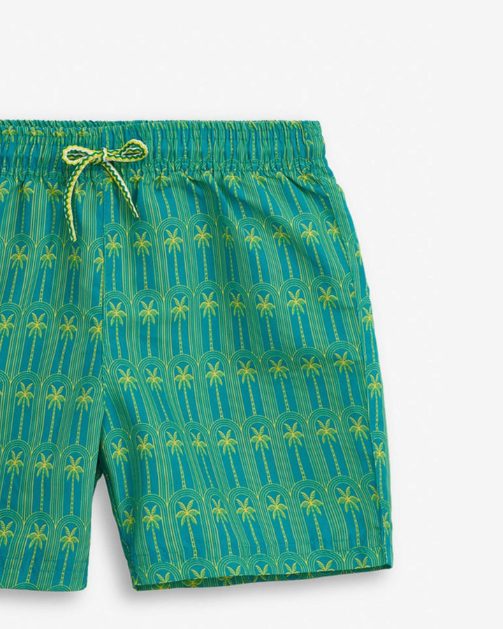 Green swim shorts with palm tree pattern on a white background