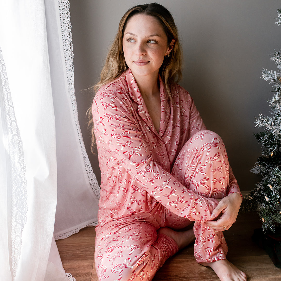 Woman in pink pajamas sitting by a window with a Christmas tree in the background