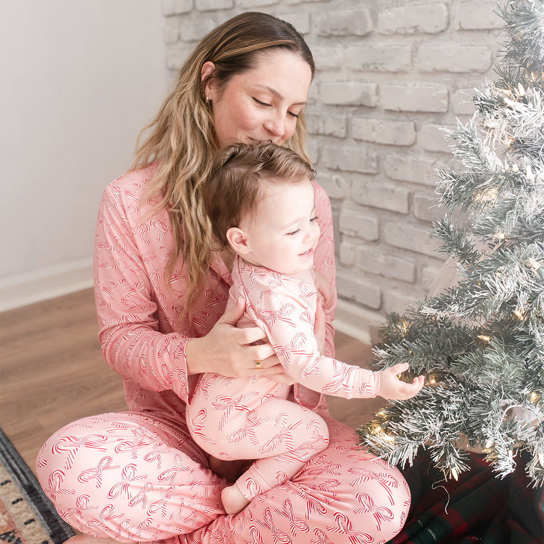 Woman and child in matching pink pajamas sitting by a decorated Christmas tree.