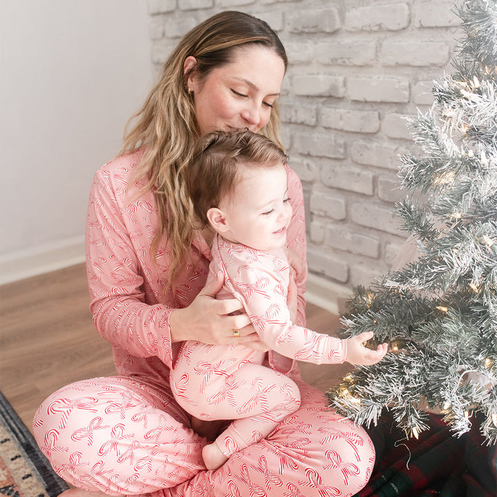 Woman and child in matching pink pajamas sitting by a decorated Christmas tree.