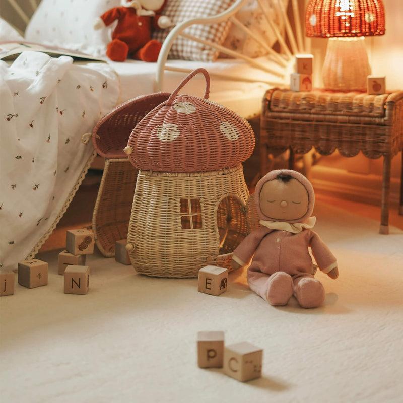 this picture shows a small dinkum doll sitting next to a mushroom basket in a small child's room. 