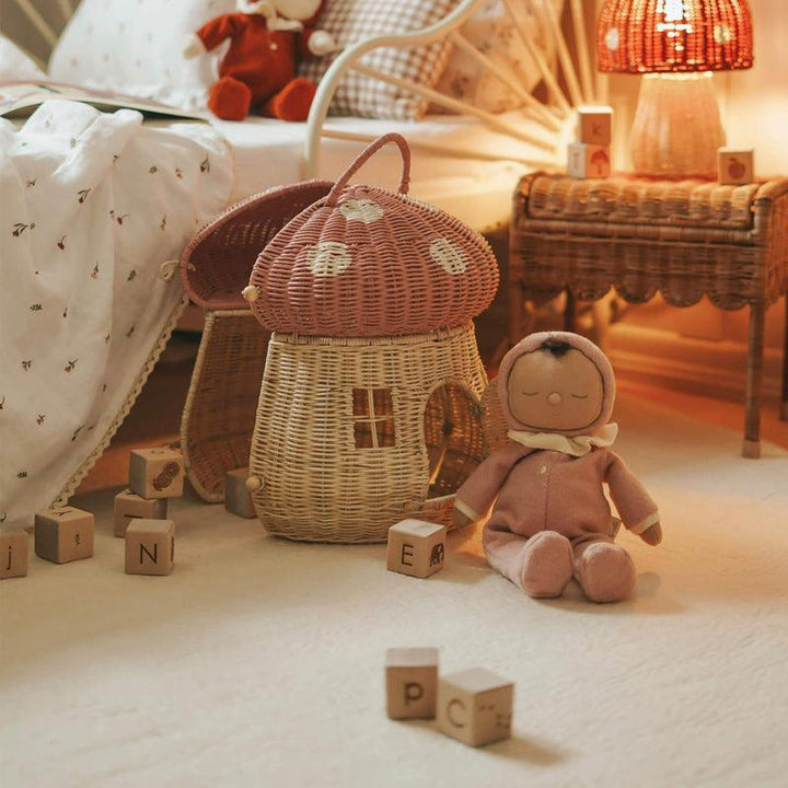 this picture shows a small dinkum doll sitting next to a mushroom basket in a small child's room. 
