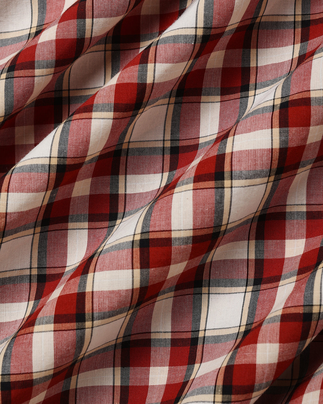 A close-up of draped plaid fabric with a red, white, and dark gray tartan pattern.