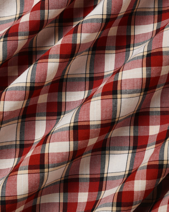 A close-up of draped plaid fabric with a red, white, and dark gray tartan pattern.