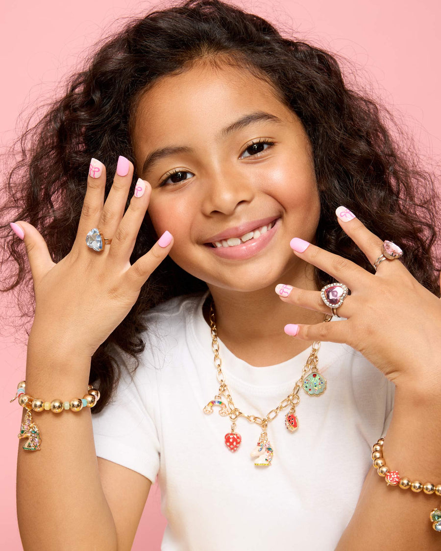 Young girl wearing multiple pieces of jewelry against a pink background