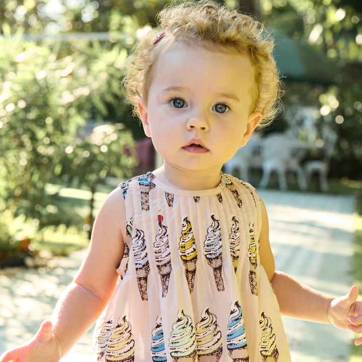 Child wearing a sleeveless dress with ice cream cone pattern outdoors