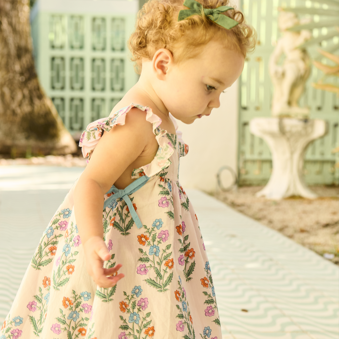 Young child in a floral dress standing outdoors with a blurred background