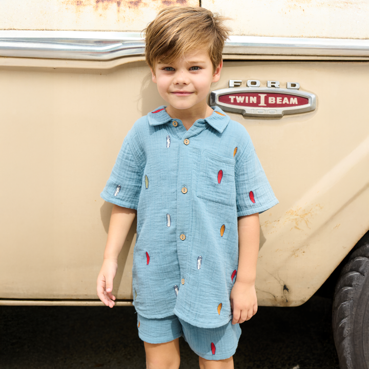 Child wearing a blue outfit with red and yellow accents in front of a vintage Ford vehicle.