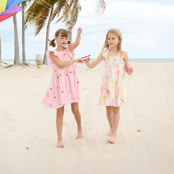 two little girls on the beach in pretty summer dresses: one pink and one with kites.