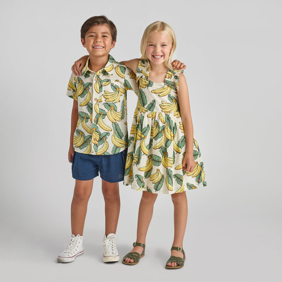 Two children wearing banana-patterned outfits on a plain background