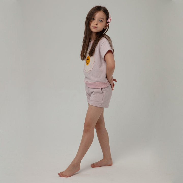 young girl modeling the daisy outfit and turned to the side. at this angle you can see the shorts have a relaxed fit and hit mid thigh and the top is a medium length and hits passed the waist. 