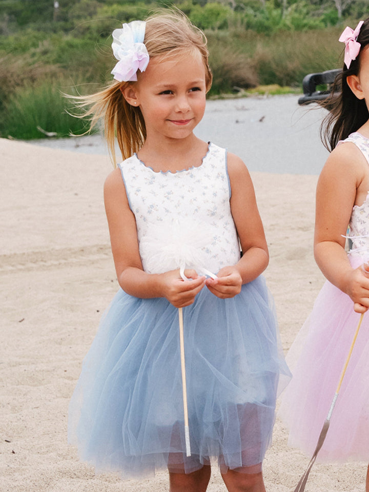 Two young girls in floral dresses standing on a sandy beach.