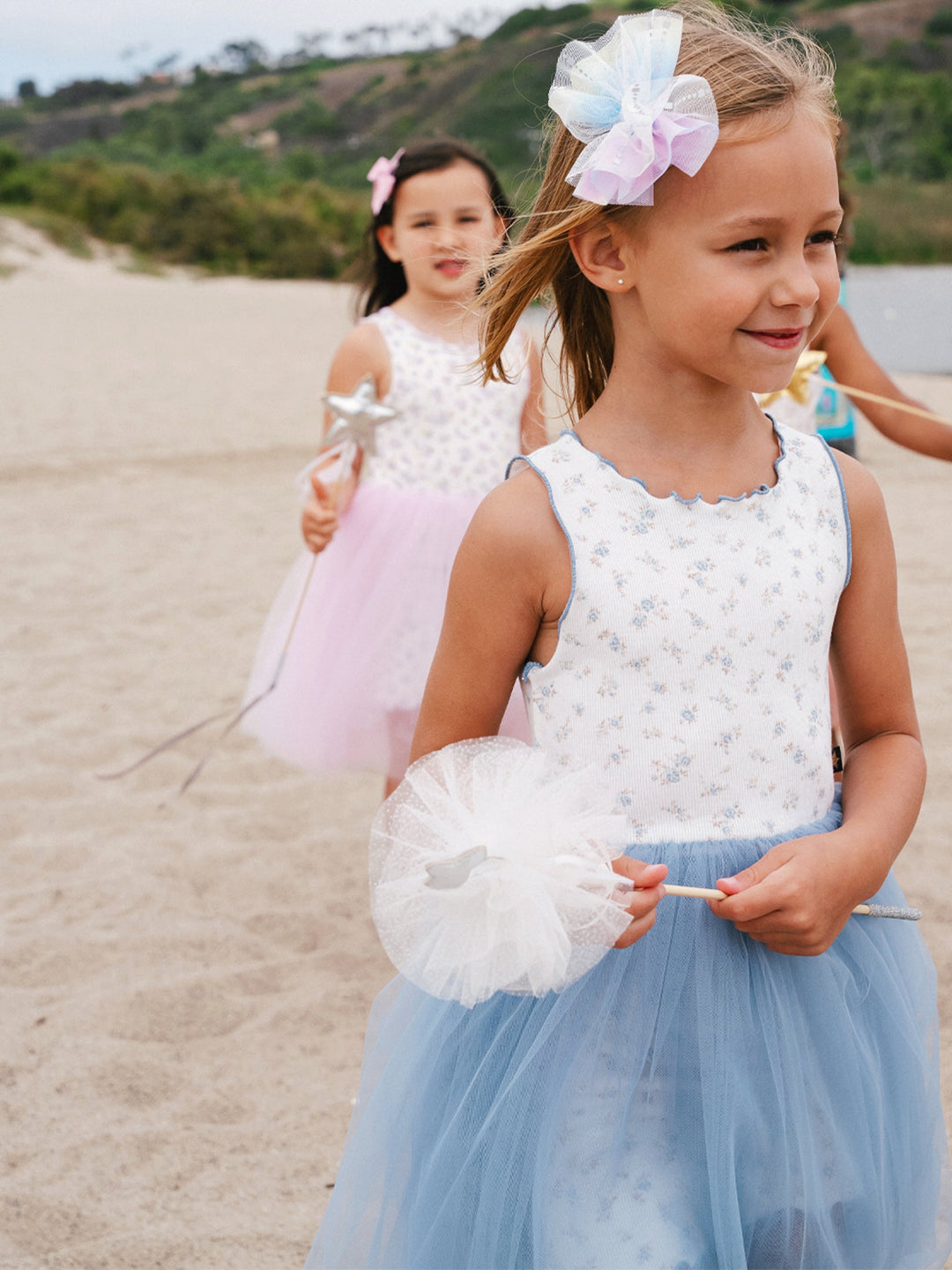 Two young girls in dresses standing on a sandy beach.