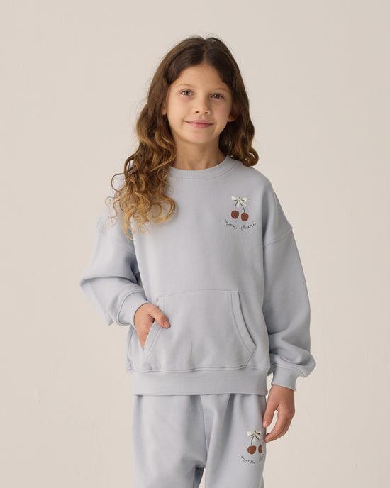 little girl modeling the sweatset in light blue with cherries at the corner of the sweatshirt 