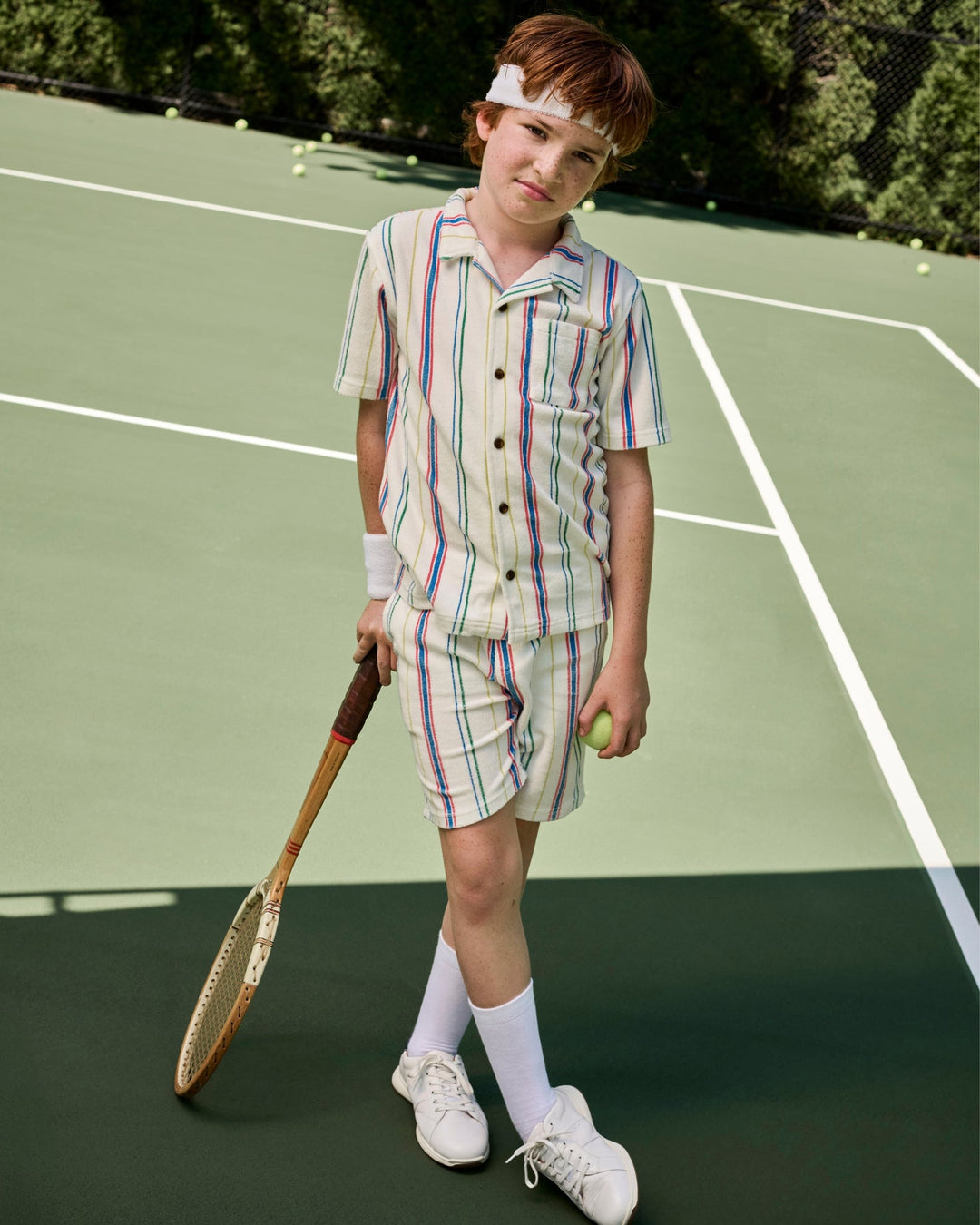 Child in vintage tennis outfit holding a racket and ball on a tennis court