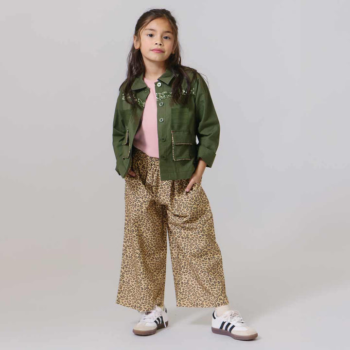 Child wearing a green jacket, pink shirt, and leopard print pants on a plain background