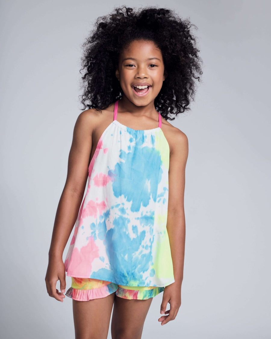 Young girl wearing a colorful tie-dye top and shorts on a gray background