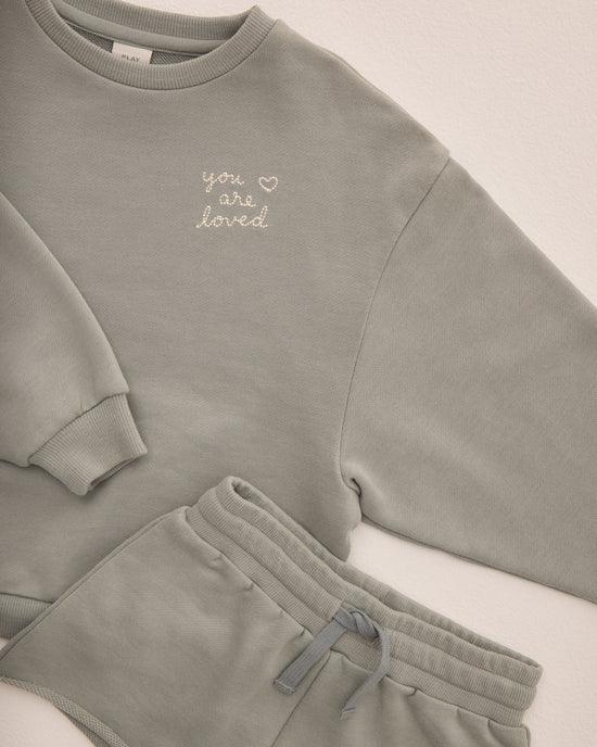 close up of the "you are loved" stitched on to the sweatshirt in the eucalyptus colored sweatshirt. 